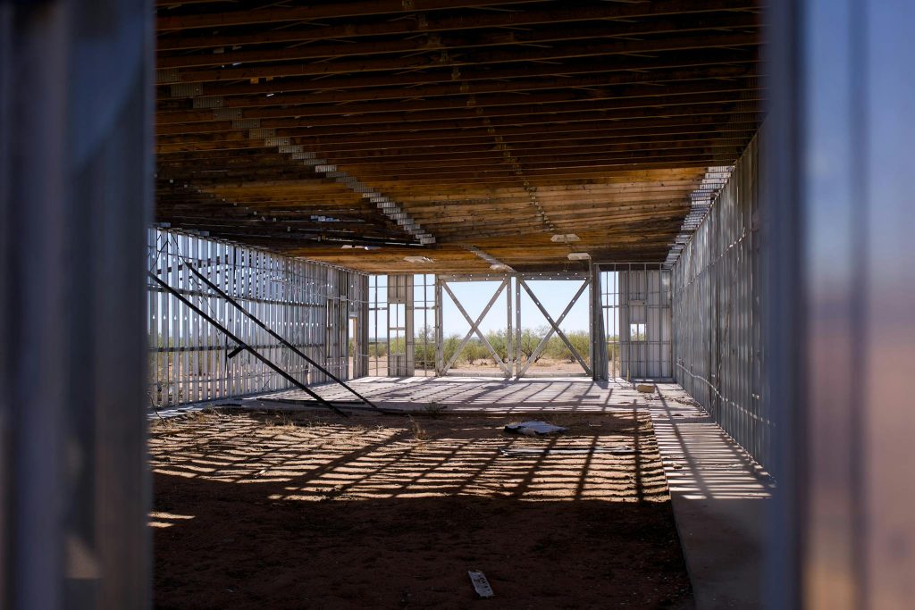 Interior view of a construction site with metal framing and wooden ceiling, under bright sunlight.